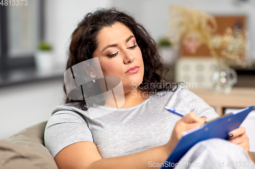 Image of young woman with clipboard taking notes at home