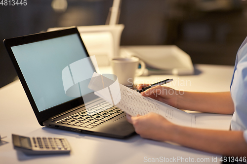 Image of woman with laptop and papers at night office