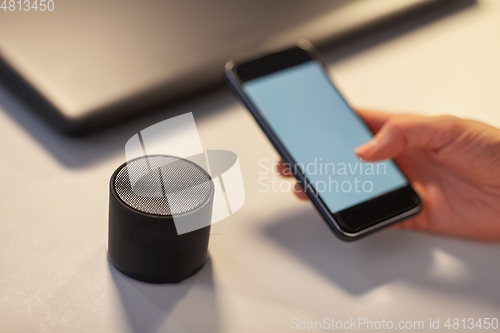 Image of hand with smartphone and smart speaker at office
