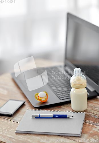 Image of baby milk formula, laptop and notebook on table