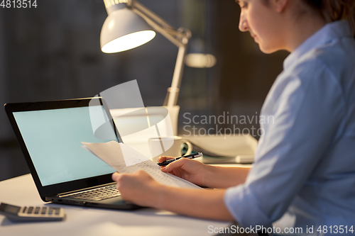 Image of woman with laptop and papers at night office