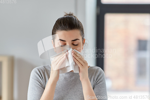 Image of sick woman blowing nose in paper tissue at home