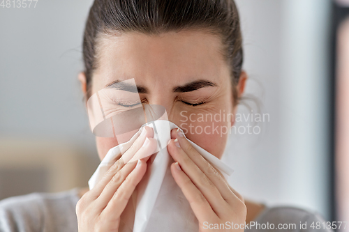 Image of sick woman blowing nose in paper tissue at home