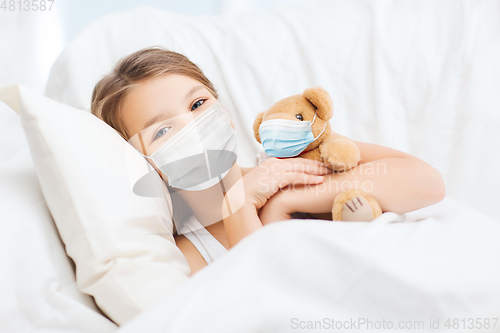 Image of girl wearing medical mask with teddy bear in bed