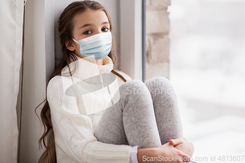 Image of sad girl in medical mask sitting on sill at home