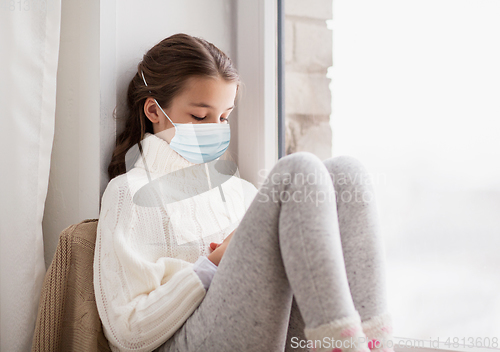 Image of sad girl in medical mask sitting on sill at home