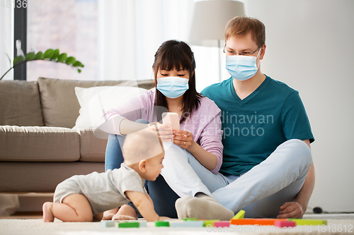 Image of family with baby in medical masks at home