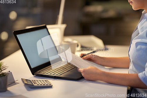 Image of woman with laptop and papers at night office