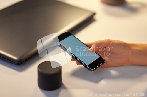 Image of hand with smartphone and smart speaker at office