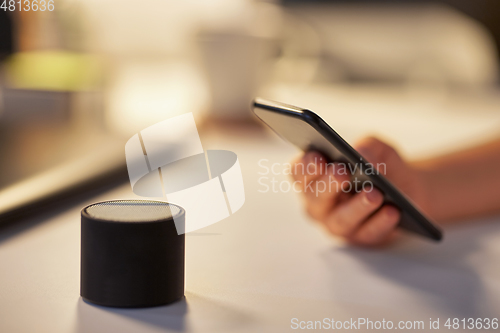 Image of hand with smartphone and smart speaker at office