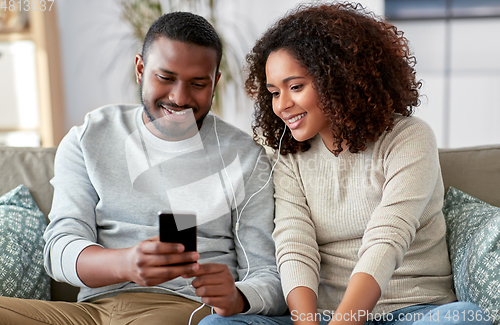 Image of happy couple with smartphone and earphones at home