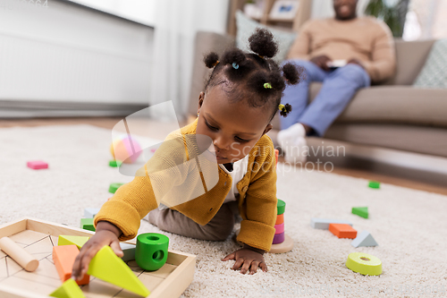 Image of african baby girl playing with toy blocks at home