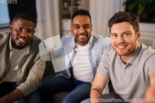 Image of happy male friends taking selfie at home