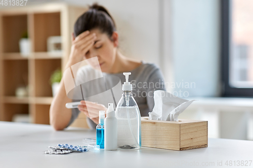 Image of medicines and sick woman with thermometer at home