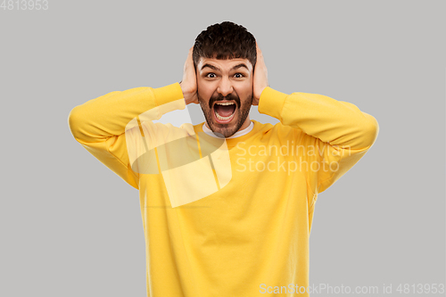 Image of man in yellow sweatshirt closing ears by hands