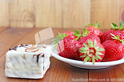 Image of ripe red strawberries on the white plate and cake