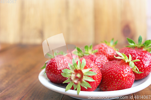 Image of ripe red strawberries on the white plate on the brown