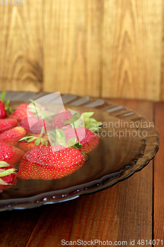 Image of ripe red strawberries in the water on the plate on the brown