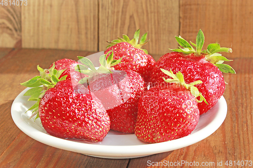 Image of ripe red strawberries on the white plate on the brown