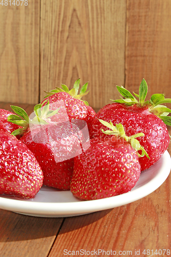 Image of ripe red strawberries on the white plate on the brown