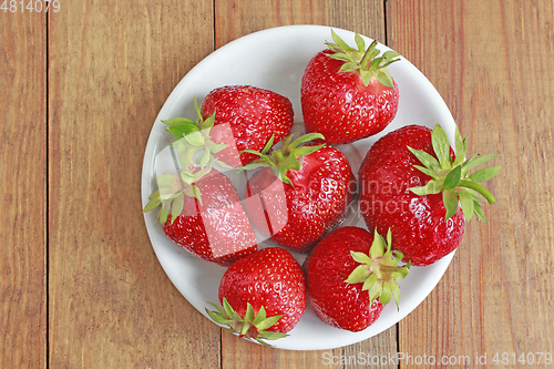 Image of ripe red strawberries on the white plate on the brown