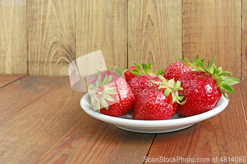 Image of ripe red strawberries on the white plate on the brown