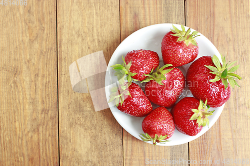 Image of ripe red strawberries on the white plate on the brown