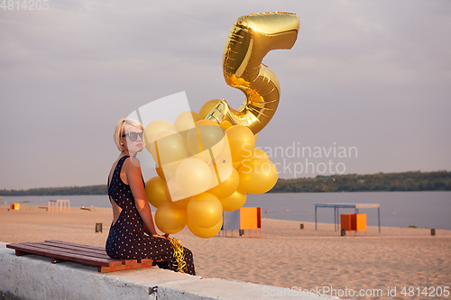 Image of Young woman with many golden balloons.