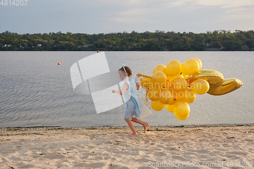 Image of Little girl with many golden balloons on the beach at sunset