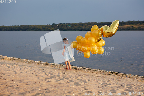 Image of Little girl with many golden balloons on the beach at sunset