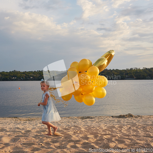 Image of Little girl with many golden balloons on the beach at sunset