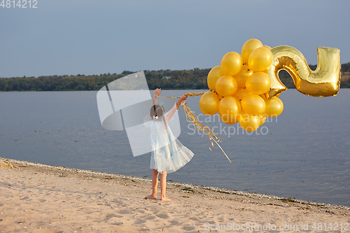 Image of Little girl with many golden balloons on the beach at sunset