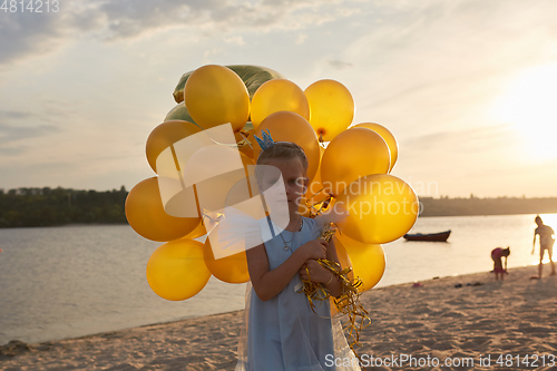 Image of Little girl with many golden balloons on the beach at sunset