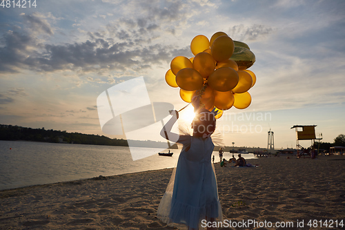 Image of Little girl with many golden balloons on the beach at sunset