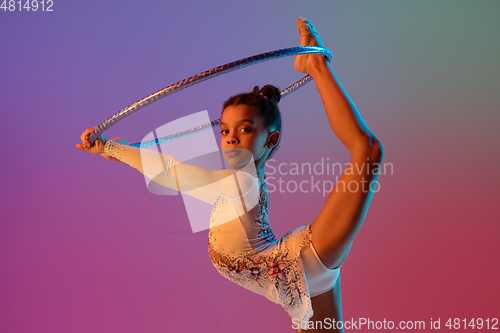 Image of African-american rhythmic gymnast, pretty girl practicing on gradient studio background in neon light