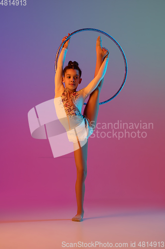 Image of African-american rhythmic gymnast, pretty girl practicing on gradient studio background in neon light