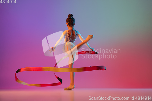 Image of African-american rhythmic gymnast, pretty girl practicing on gradient studio background in neon light