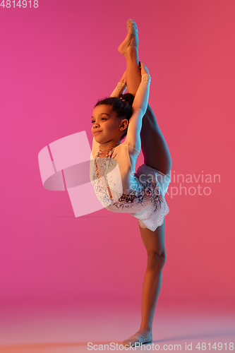 Image of African-american rhythmic gymnast, pretty girl practicing on gradient studio background in neon light