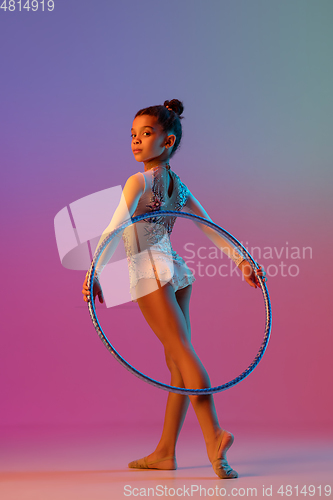 Image of African-american rhythmic gymnast, pretty girl practicing on gradient studio background in neon light