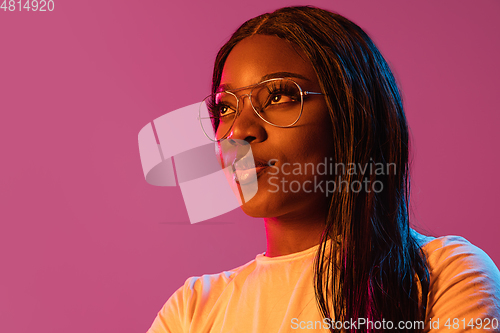 Image of African young woman\'s portrait on pink studio background in neon. Concept of human emotions, facial expression, youth, sales, ad.