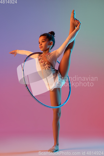 Image of African-american rhythmic gymnast, pretty girl practicing on gradient studio background in neon light