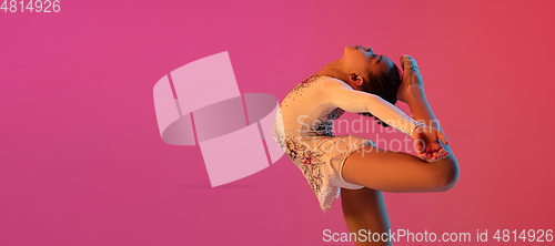 Image of African-american rhythmic gymnast, pretty girl practicing on gradient studio background in neon light