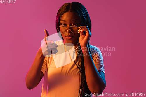 Image of African young woman\'s portrait on pink studio background in neon. Concept of human emotions, facial expression, youth, sales, ad.