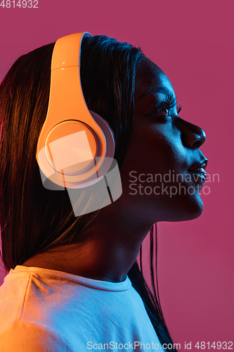 Image of African young woman\'s portrait on pink studio background in neon. Concept of human emotions, facial expression, youth, sales, ad.