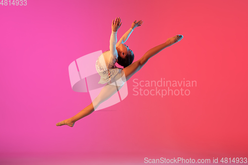 Image of African-american rhythmic gymnast, pretty girl practicing on gradient studio background in neon light