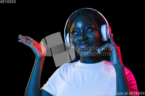 Image of African young woman\'s portrait on dark studio background in neon. Concept of human emotions, facial expression, youth, sales, ad.