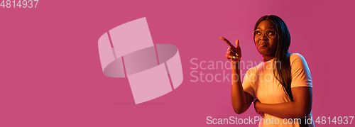 Image of African young woman\'s portrait on pink studio background in neon. Concept of human emotions, facial expression, youth, sales, ad.