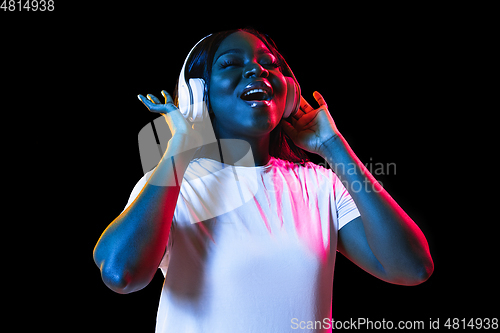 Image of African young woman\'s portrait on dark studio background in neon. Concept of human emotions, facial expression, youth, sales, ad.