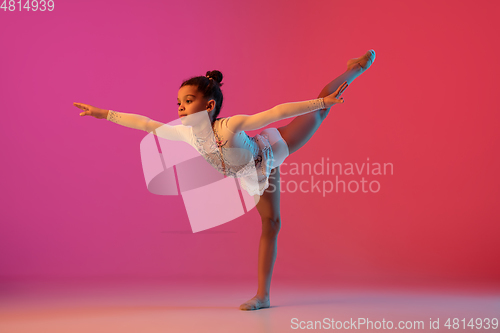 Image of African-american rhythmic gymnast, pretty girl practicing on gradient studio background in neon light