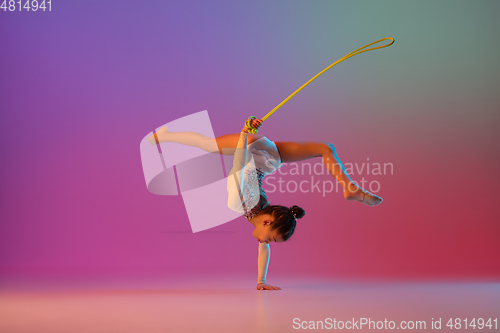 Image of African-american rhythmic gymnast, pretty girl practicing on gradient studio background in neon light